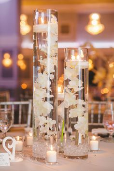 two tall clear vases with flowers and candles are on the table in front of each other