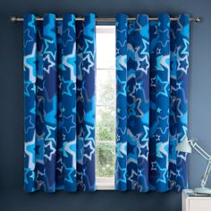 a blue curtain with stars on it hanging in front of a window next to a lamp