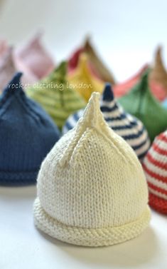 several knitted hats are lined up on a white counter top, with the caps in different colors