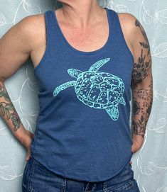 Our hand-drawn Sea Turtle design is printed in teal on this super soft royal blue eco tri-blend racerback tank. Straight through the body. Overlock hem. 40% tencel model (plant fibers), 35% cotton, 25% recycled poly. Sizes available: XS, SM, MED, LRG, XL, 2X.  Runs true to size for form fitting, order up for a looser fit.  Model is a size Medium/ Large and wearing a medium. Our original, hand-drawn designs are printed on sweat-shop free clothing using environmentally conscious water-based inks. Fitted Casual Tank Top With Screen Print, Casual Fitted Tank Top With Screen Print, Blue Crew Neck Tank Top For Beach, Blue Crew Neck Tank Top For The Beach, Casual Blue Printed Tank Top, Blue Cotton Racerback Tank Top, Blue Graphic Print Racerback Tank Top, Blue Racerback Tank Top With Graphic Print, Blue Racerback Top With Graphic Print