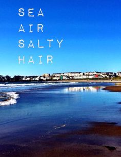 the words sea air salty hair are written in white on a blue sky background over an ocean beach