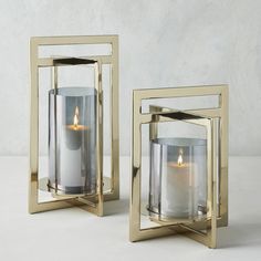 two square candle holders with one lit and the other empty, sitting on a white surface