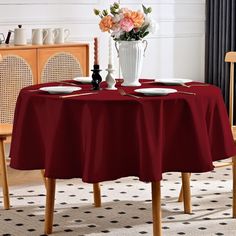 a dining room table with red cloths and white plates on it, in front of a vase filled with flowers