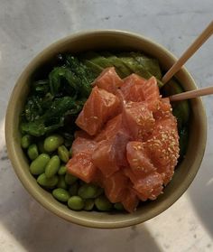 a bowl filled with meat and vegetables on top of a white counter next to chopsticks