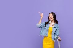 a woman in a yellow dress and denim jacket is pointing at something with her finger