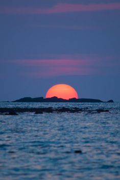 the sun is setting over an island in the middle of the ocean as seen from across the water