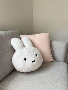 a white stuffed animal sitting on top of a gray couch next to a pink pillow