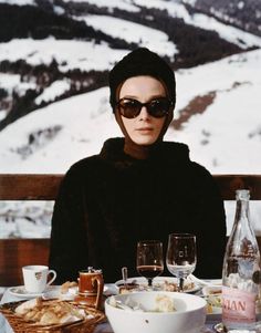 a woman wearing sunglasses sitting at a table with food and drinks in front of her