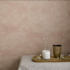 a table with a candle, cup and spoon on it in front of a wall