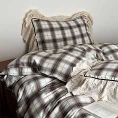 an unmade bed with a plaid comforter and book on the end table next to it