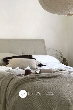 a bed with white sheets and pillows in a bedroom next to a wall mounted light