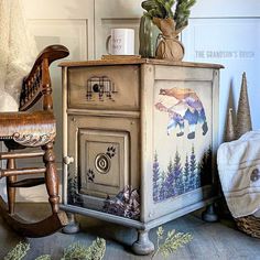 an old fashioned wooden cabinet painted with bear images and pine cones on top, next to a rocking chair