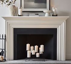 a fireplace with white candles in front of it and a painting on the wall above