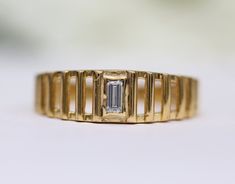 a gold ring with an emerald cut diamond in the center, sitting on a white surface