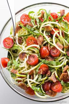 a glass bowl filled with salad topped with meat and veggies, on top of a white table