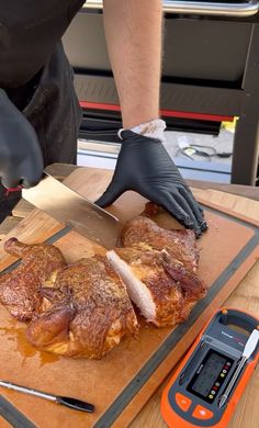 a person cutting meat with a knife on a cutting board next to a calculator