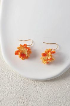 two orange and yellow flower earrings sitting on top of a white plate next to each other