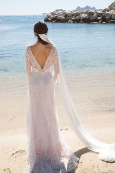 a woman standing on top of a beach next to the ocean wearing a wedding dress