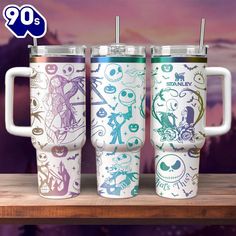 three travel mugs sitting on top of a wooden table in front of a purple background