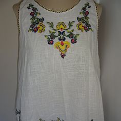 A Women's Max Studio Top. Size L. Nwt (New With Tags). A White, Sleeveless Top With Embroidered Flowers Around The Collar And Down The Front And The Front Hem With A Crochet And Fringe Hem. The Collars And Arms Have Blue And Yellow Trim And There Are Blue And Yellow Ties With Tassels On The Back. 100% Cotton. Approximate Measurements (Not Body Measurements): Bust 40", And From Shoulder To Hem 22-1/2" Summer Tops With Contrast Embroidery, Yellow Folk Top With Floral Embroidery, Yellow Folk Style Top With Floral Embroidery, Yellow Floral Embroidered Folk Top, Yellow Folk Style Blouse For Spring, Yellow Folk Style Spring Blouse, Wide Sleeve Top, Womens Printed Tops, Yellow Floral Top