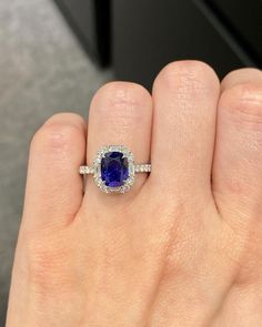 a woman's hand holding a ring with an oval shaped blue sapphire surrounded by diamonds