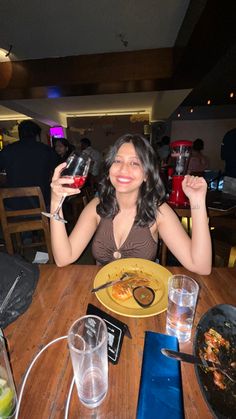 a woman sitting at a table holding up two wine glasses