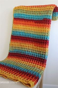 a multicolored crocheted blanket sitting on top of a white chair