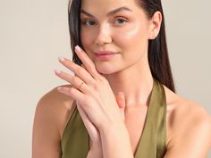 a woman in a green dress holding her hand up to her face and looking at the camera