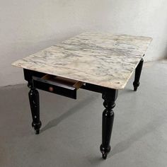 a marble top table with black legs and drawers on the bottom, against a white wall