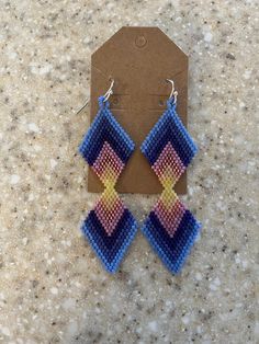 Native American-made beaded large double diamond shaped earrings in chevron design of blues, purple, pinks and yellow. Measures 3" long x 1" wide, stainless steel hooks with rubber backings. Handmade Blue Geometric Earrings, Bohemian Blue Geometric Earrings, Multicolor Beaded Geometric Earrings, Native Earrings, Yellow Chevron, Diamond Shape Earrings, Double Diamond, Earrings Large, Chevron Design