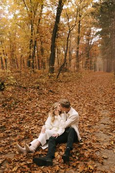 a man and woman sitting on the ground surrounded by fallen leaves in an autumn forest