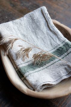 a wooden bowl with a towel and some feathers in it on top of a table