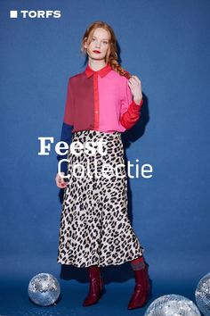 a woman standing in front of a blue background wearing a leopard print skirt and pink shirt