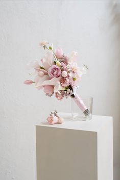 a bouquet of pink flowers sitting on top of a white table next to a glass vase