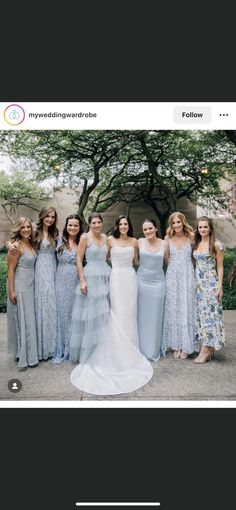 a group of women in dresses standing next to each other on a sidewalk with trees behind them