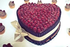 a heart shaped chocolate cake with raspberries on top and gold ribbon around the edges