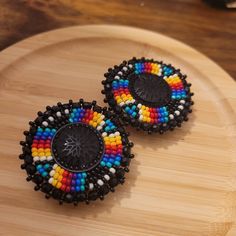 These earrings are made with seed beads and black centers encircled in black rhinestone. They are then branded with our logo, backed with moose hide and your choice of earring findings. The edging is done with black rondelle beads, creating and extra bit of sparkle as the earrings move about. Each pair are made with hypoallergenic materials for sensitive ears. You can now upgrade your earring to include a tassel attachment. This upgrade allows you to have a 3 in 1 pair of earrings. The tassel ea Beaded Earrings With Cabochon Centers, Round Beaded Earrings, Indigenous Beading, Indigenous Style, Native Beading, Seed Bead Jewelry Patterns, Native Beading Patterns, Beaded Earrings Native, Tassel Earring