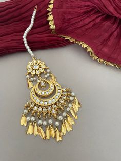 A bridal, kundan tika as part of your wedding jewelry you'll love! Shimmering kundan stones encrust the setting of this pretty maang tika with pipal patti drops strung with lustrous pearls.  Details: Length-8Inches Width-2.25 Inches All products are manufactured using traditional skills from our rich heritage of crafts.  The process of these crafts is essentially manual. Hence, any irregularities or variations are an inherent part of these handcrafting processes. White Cutdana Jhumkas For Wedding, Wedding White Cutdana Jhumkas, Gold Chandbali Tikka With Zari Work, Navratri Bridal Earrings With Meenakari Details, Bridal Earrings With Latkans For Navratri Wedding, Ceremonial Bridal Cutdana Earrings For Diwali, White Chandbalis For Wedding And Diwali, Bollywood Bridal Sets With Latkans For Festive, Ceremonial Kundan Bridal Earrings With Stone Work