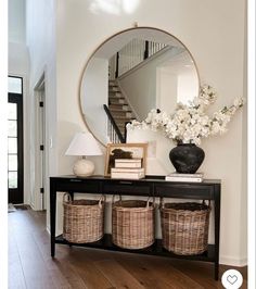 a black console table with baskets and flowers on it in front of a large round mirror