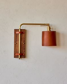 a wall light with a leather shade hanging from it's side on a white wall