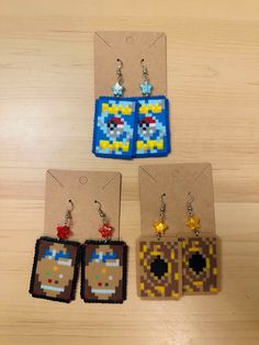 three pixel earrings are shown on a wooden table next to an earring with the video game character pacman