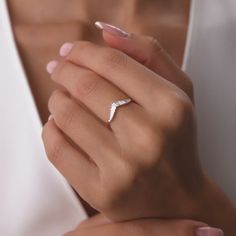 a woman's hand with a diamond ring on her left hand, wearing a white shirt