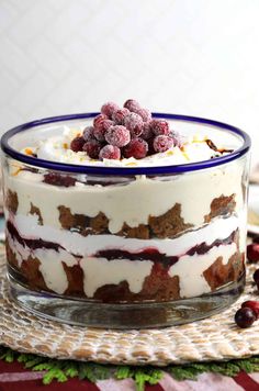 a layered cake with berries and whipped cream in a glass dish on top of a table