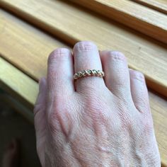 a person's hand with a gold ring on their left hand, sitting next to a wooden bench