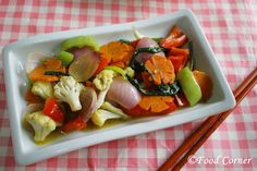 a white plate topped with vegetables and chopsticks next to a pink checkered table cloth