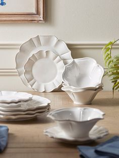 a table topped with lots of white dishes next to a potted plant on top of a wooden table