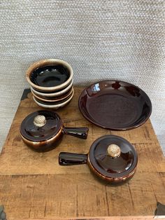 a wooden table topped with lots of brown plates and pans covered in saucers