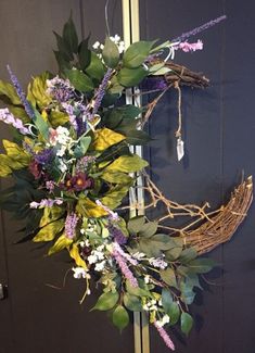 a wreath with purple flowers and greenery hangs on a door handle in front of a blue door