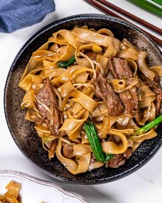 a bowl filled with beef and noodles next to chopsticks on a white table