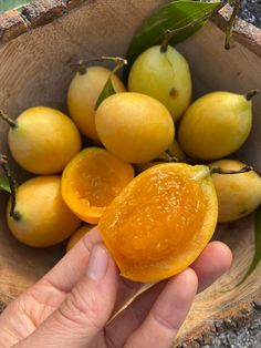 a person is holding an orange in a wooden bowl with other fruit on the table